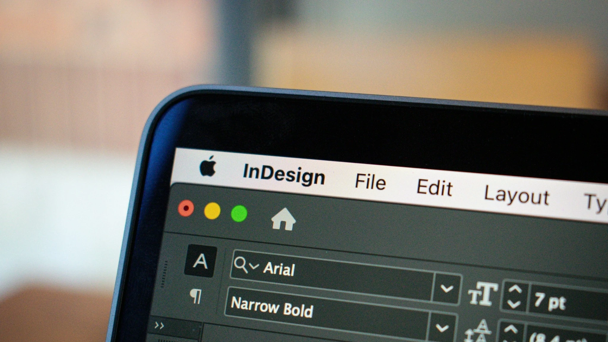Nahaufnahme eines Bildschirms mit geöffneter Adobe-InDesign-Oberfläche. Sichtbar sind der InDesign-Schriftzug in der Menüleiste sowie geöffnete Typografie- und Bedienfelder.
